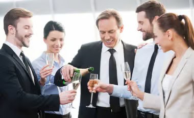 Up to 100 Guests Group of business professionals in suits celebrating with champagne at an office gathering.